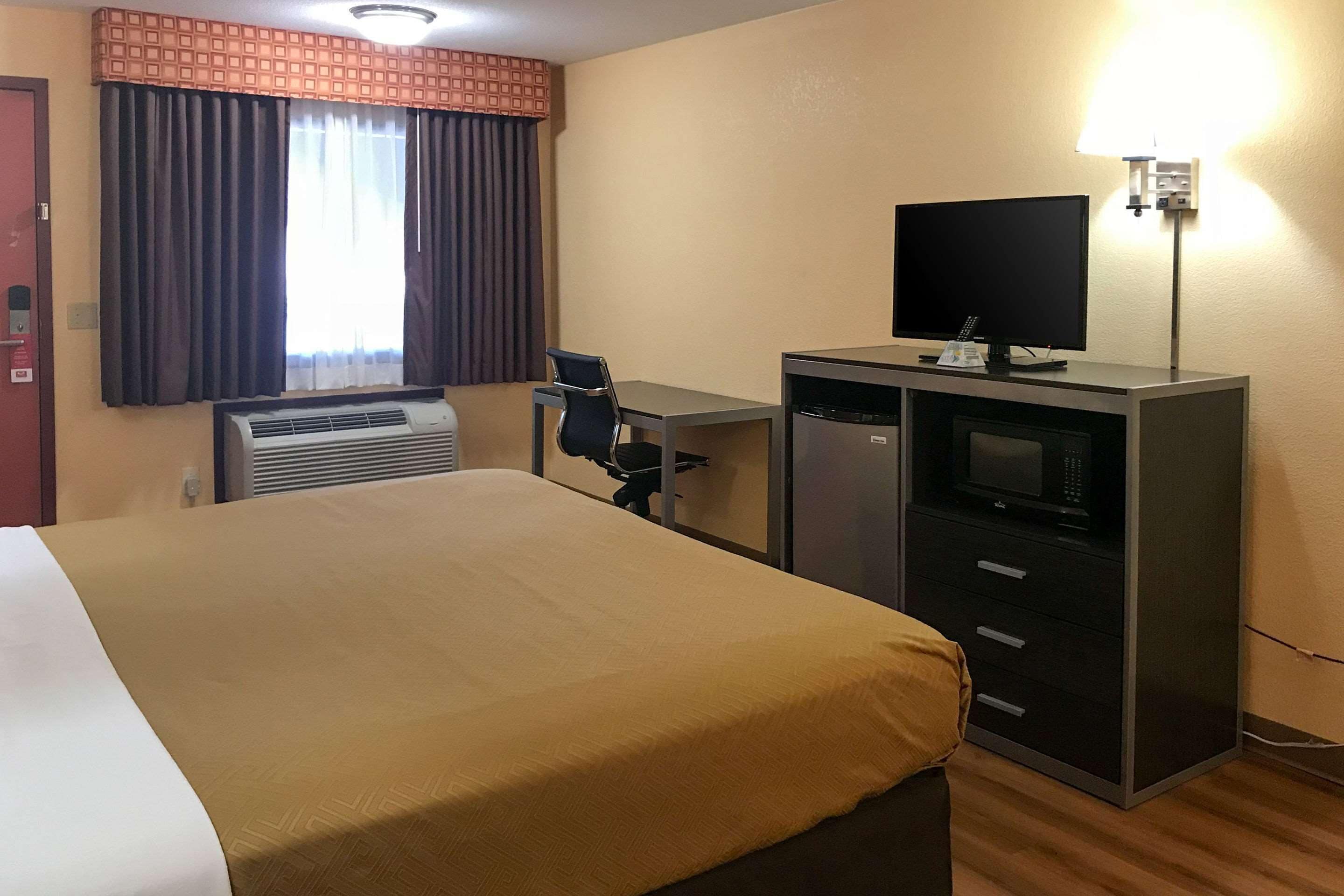 Una habitación de hotel con cama, escritorio, televisor y aire acondicionado.