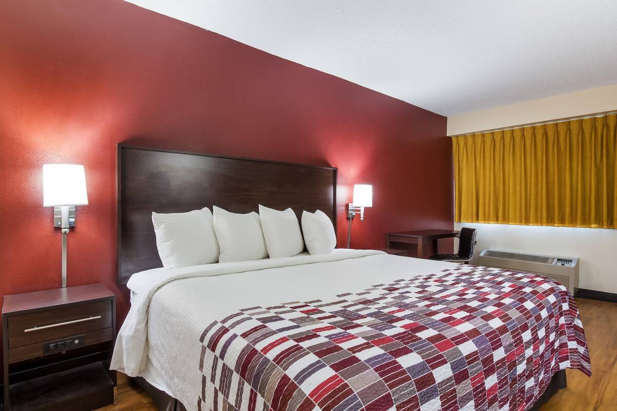 A hotel room with a large bed, two bedside tables, a nightstand, a desk, and a window with yellow curtains.