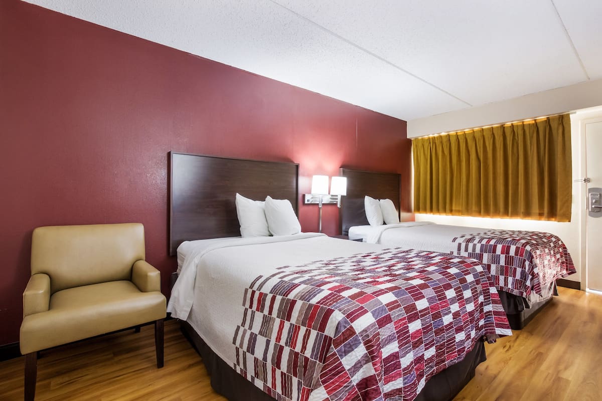 A hotel room with two beds, a chair, and a wooden floor.