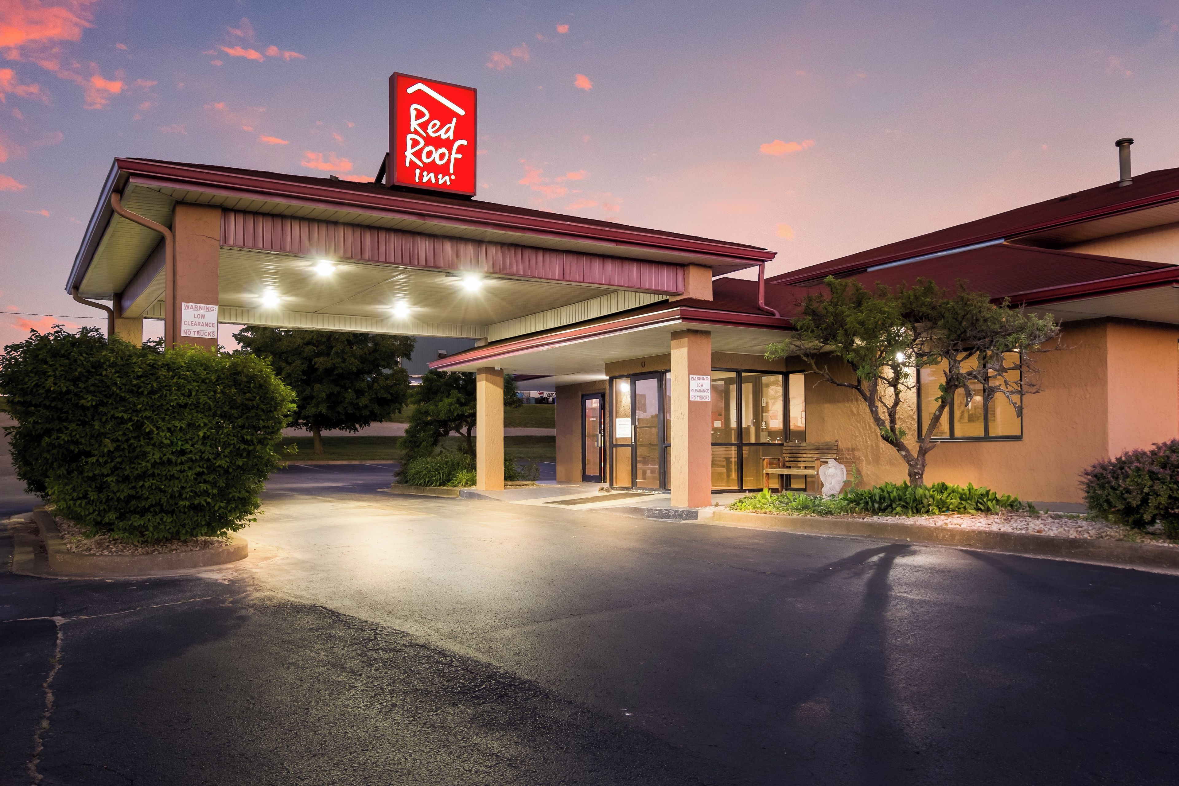 Ein Red Roof Inn mit überdachtem Parkplatz, blauem Himmel und gut beleuchtetem Eingang.