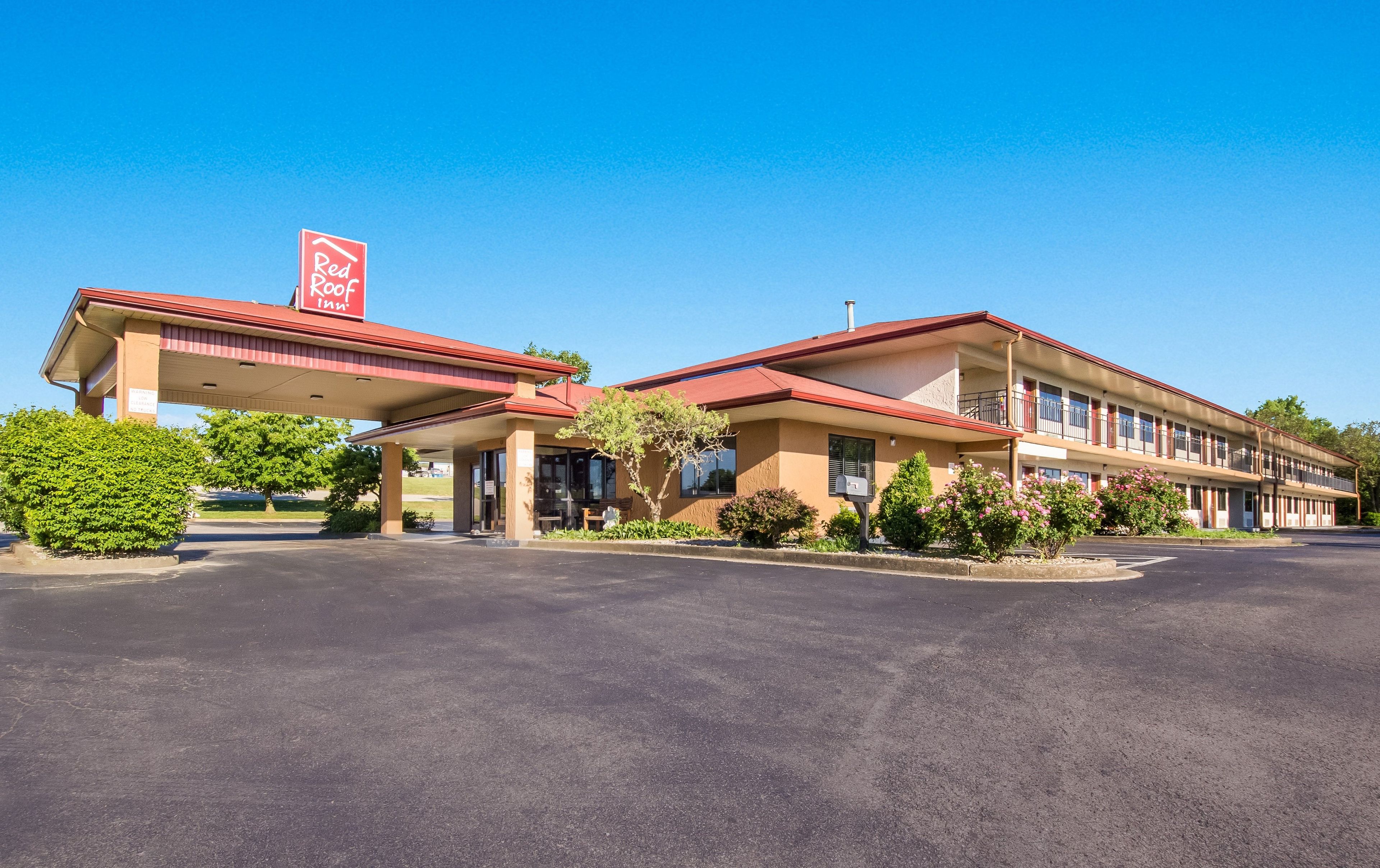 A Red Roof Inn with a two-story building, a covered parking area, and a clear blue sky.