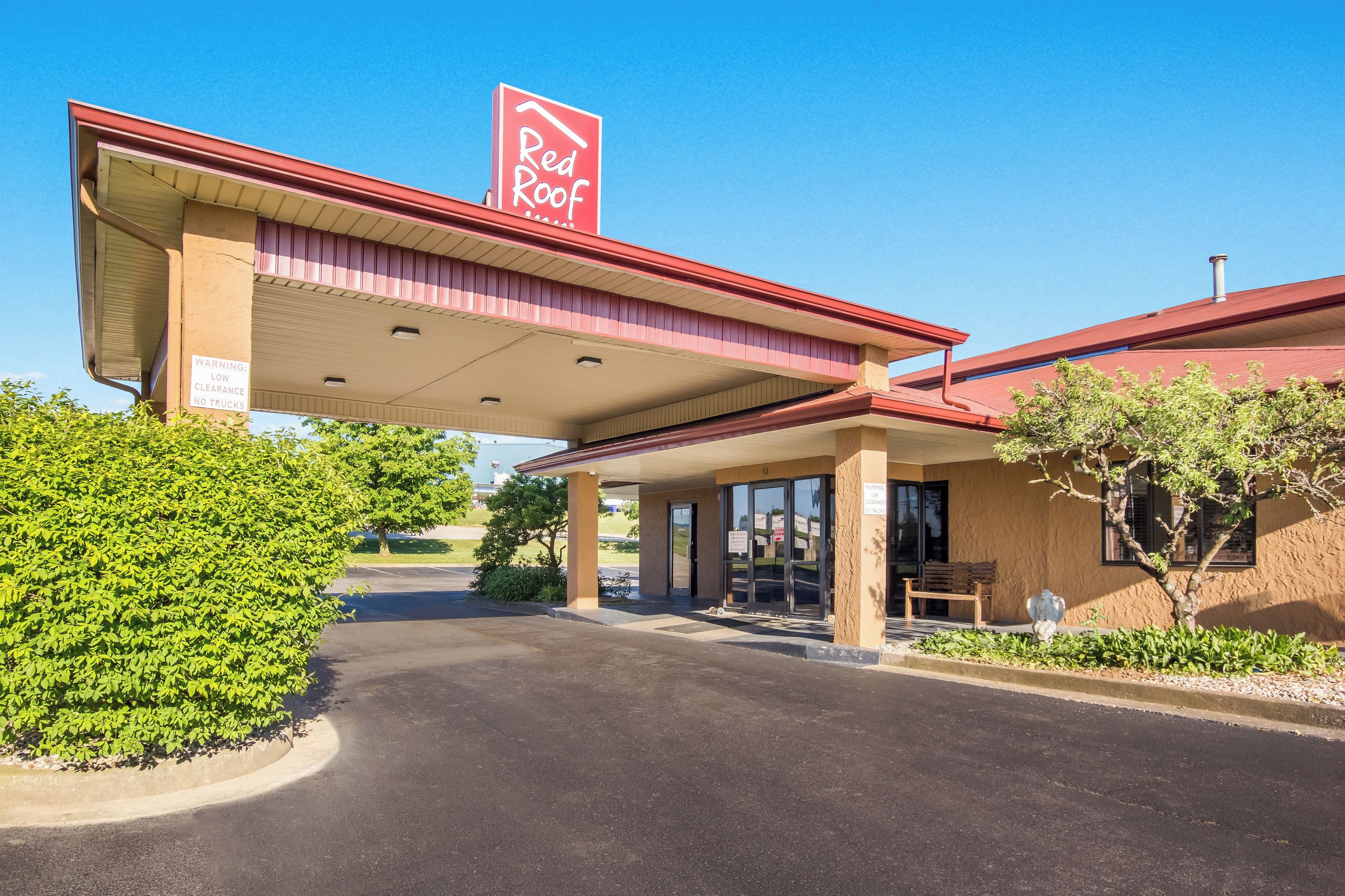 A Red Roof Inn with a covered parking area, a clear sky, and a well-maintained landscape.