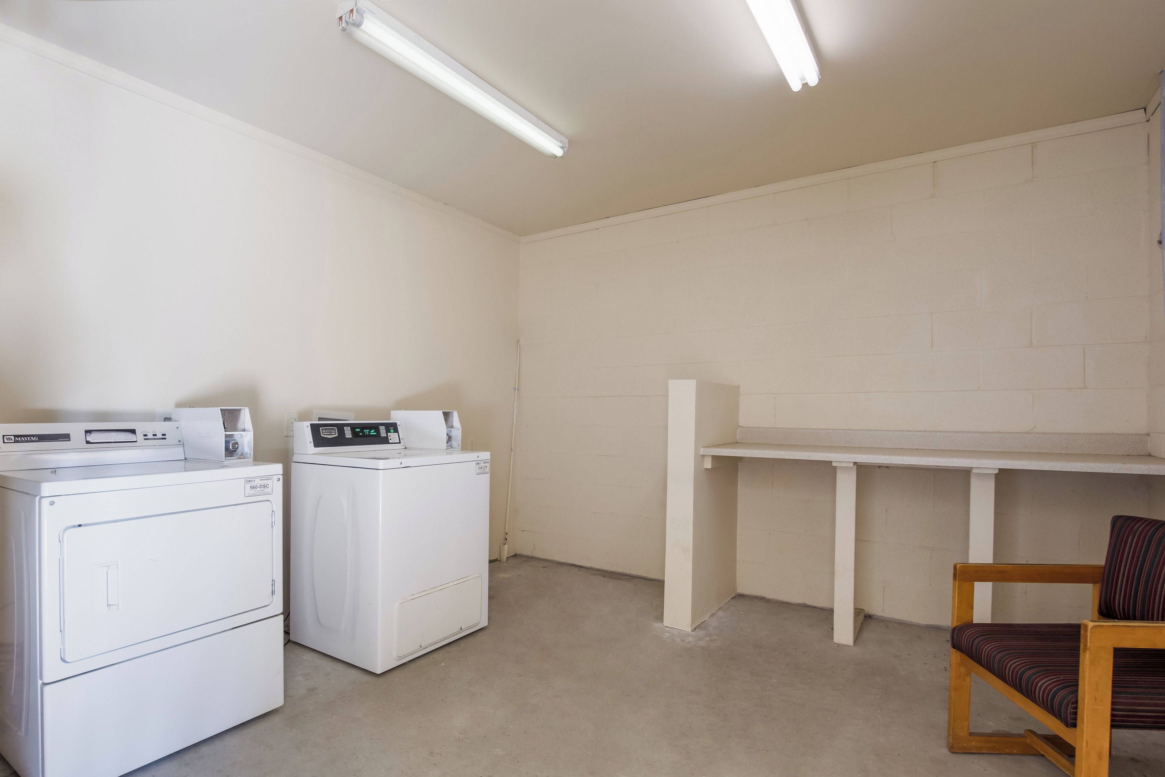 Un cuarto de lavandería con dos lavadoras, un tendedero y una silla.