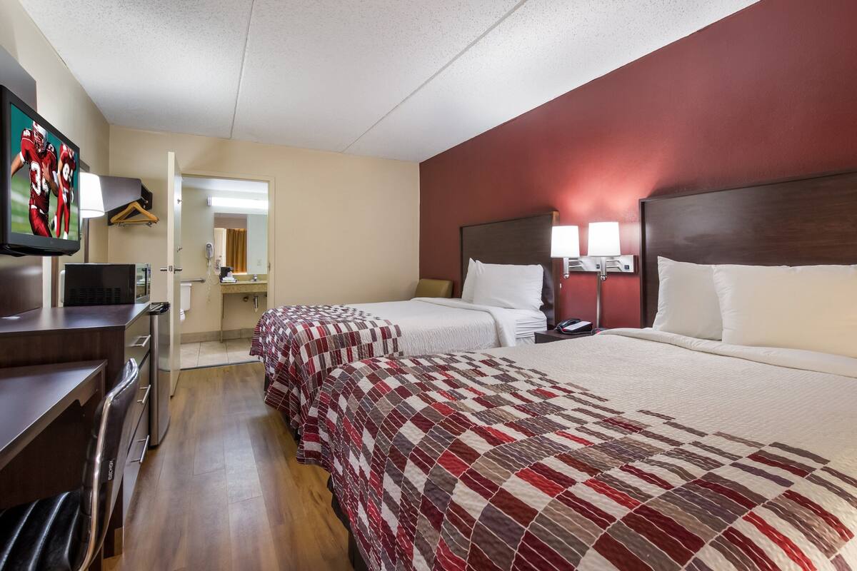 A hotel room with two beds, a desk, a TV, and a mirror.