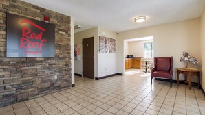 A spacious living area with a kitchen in the background, a red leather chair, and a wall-mounted sign. - Red Roof Inn Shelbyville (Shelbyville)