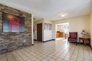 Un vaste espace de vie avec une cuisine à l’arrière-plan, un fauteuil en cuir rouge et un panneau fixé au mur.