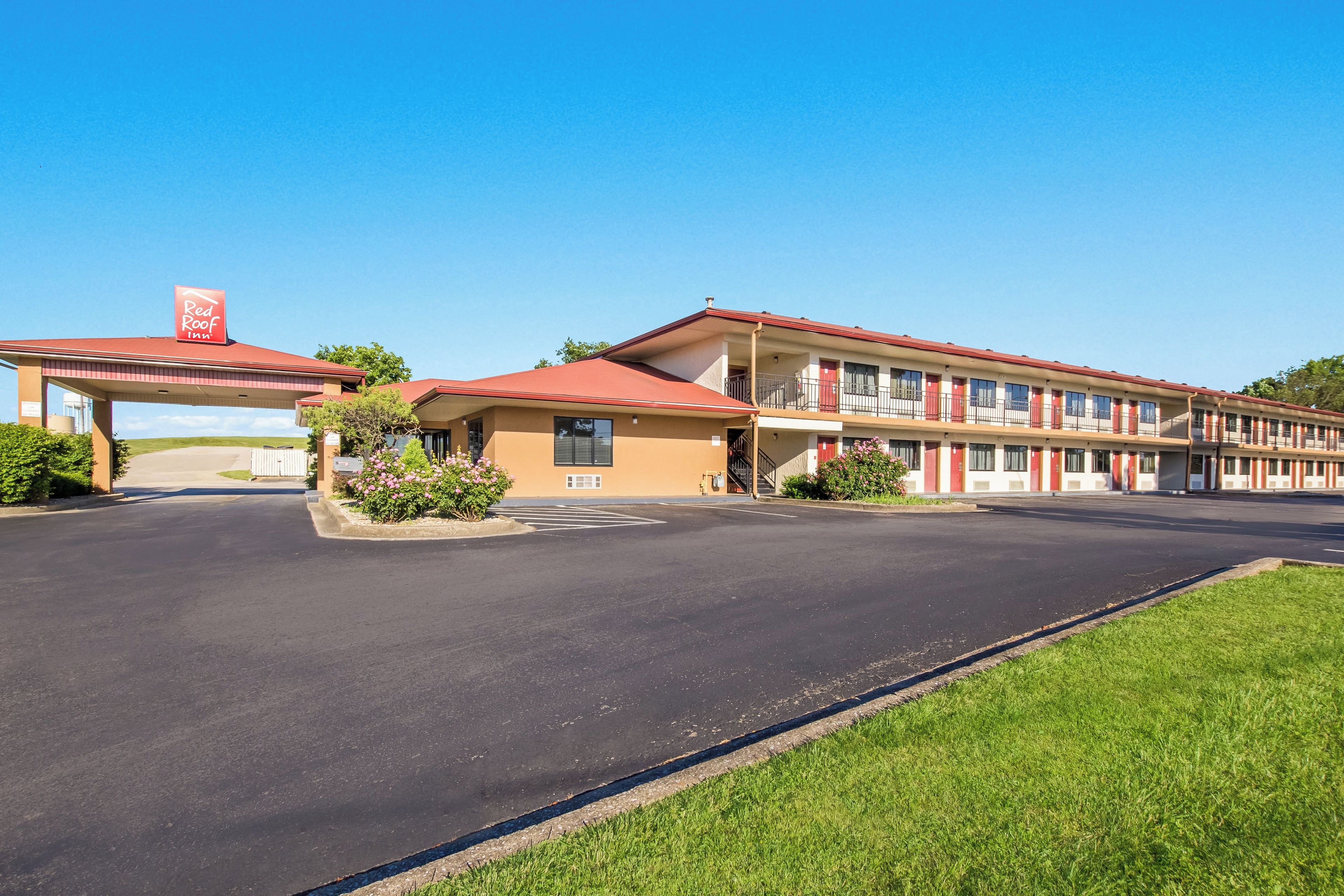 A motel with a red roof, a covered parking area, and a grassy lawn.
