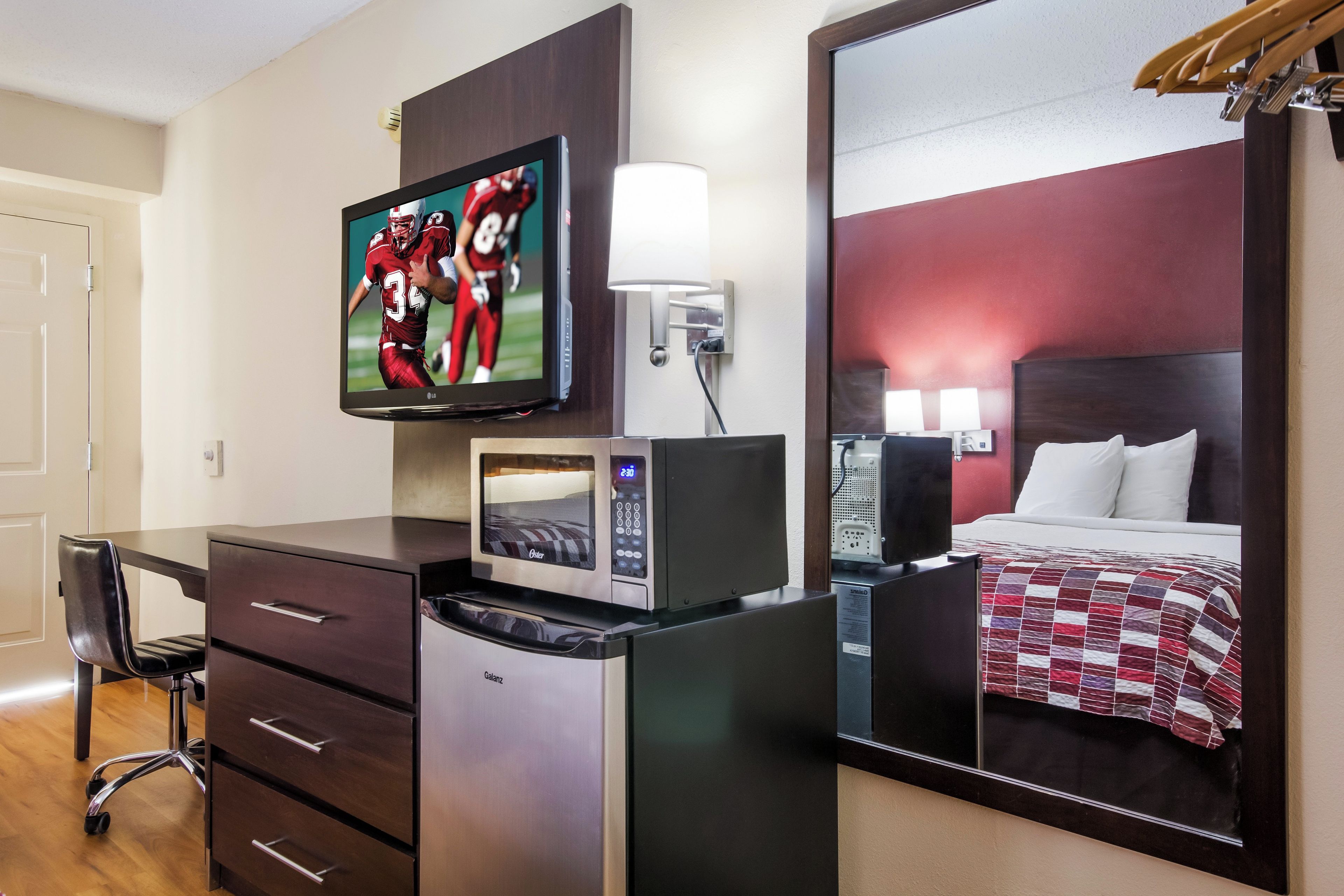 A hotel room with a bed, a desk with a chair, a television, a microwave, and a mirror.