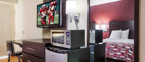 A hotel room with a bed, a desk with a chair, a television, a microwave, and a mirror.