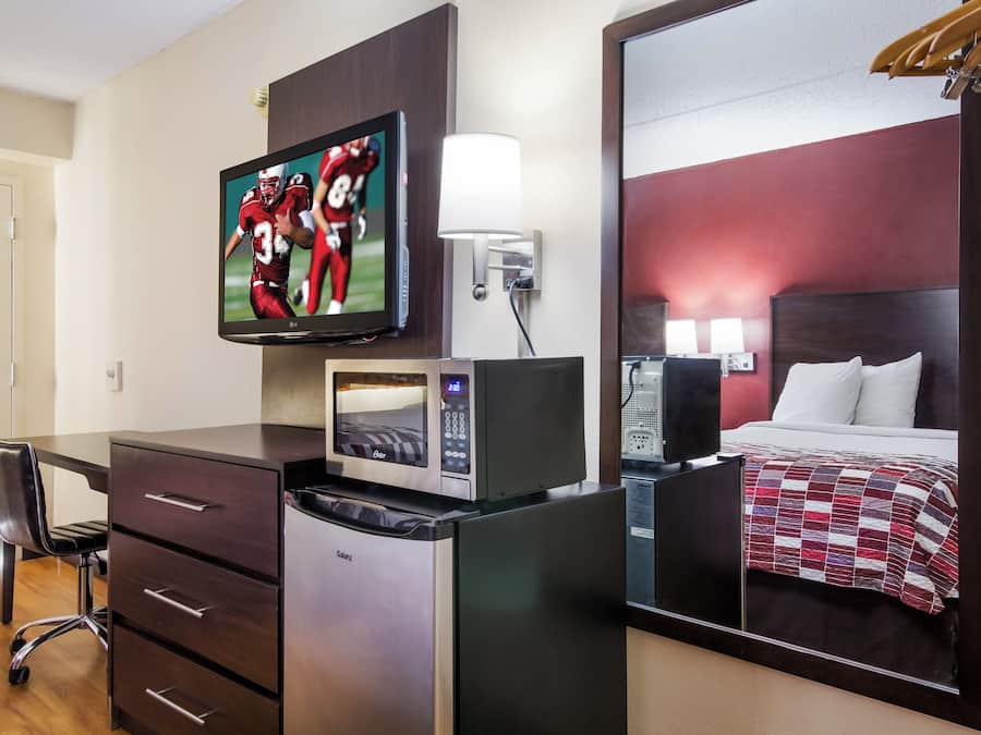 Une chambre d’hôtel équipée d’un lit, d’un bureau avec une chaise, d’une télévision, d’un four à micro-ondes et d’un miroir.