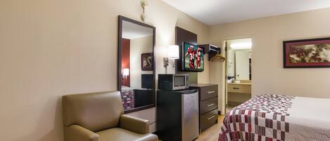 Una habitación de hotel con cama, escritorio, silla, televisor, microondas y refrigerador.