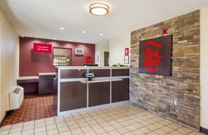 Een hotel receptie met een digitale klok, een bord met 'Gratis WiFi in alle kamers' en een 'Red Roof Inn' bord.