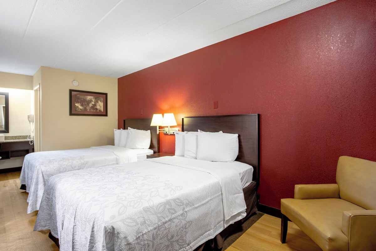 A hotel room with two beds, a chair, a lamp, and a painting on the wall.