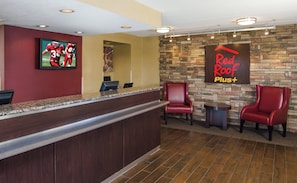 A reception area with a counter, a framed sports picture, a Red Roof Plus+ sign, and leather chairs. - Red Roof Inn PLUS+ Baltimore-Washington DC/BWI Airport (Linthicum Heights)