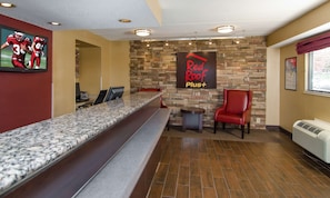 A reception area with a stone wall, a red chair, a counter with a computer, and a sign that reads 'Red Roof Plus+'. - Red Roof Inn PLUS+ Baltimore-Washington DC/BWI Airport (Linthicum Heights)