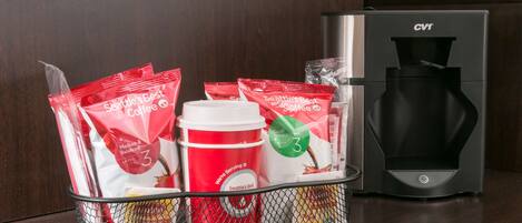 Una cafetera, una cesta con cápsulas de café y un vaso desechable.