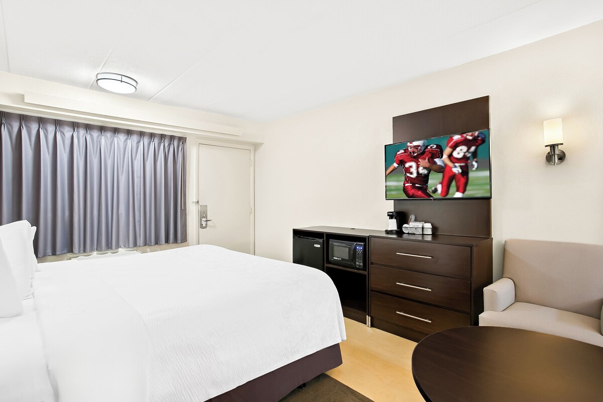 A hotel room with a large bed, a desk with a microwave, a TV on the wall, and a sofa.