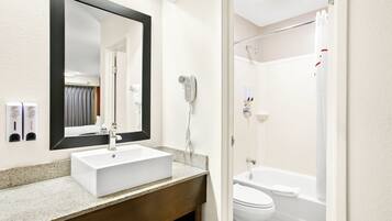 A bathroom with a white sink, a large mirror, a handheld showerhead, and a toilet.