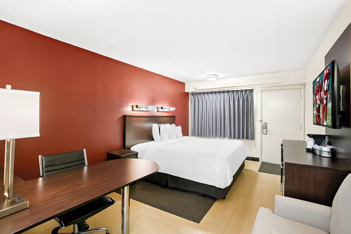 A hotel room with a bed, a desk, a chair, a television, and a door.