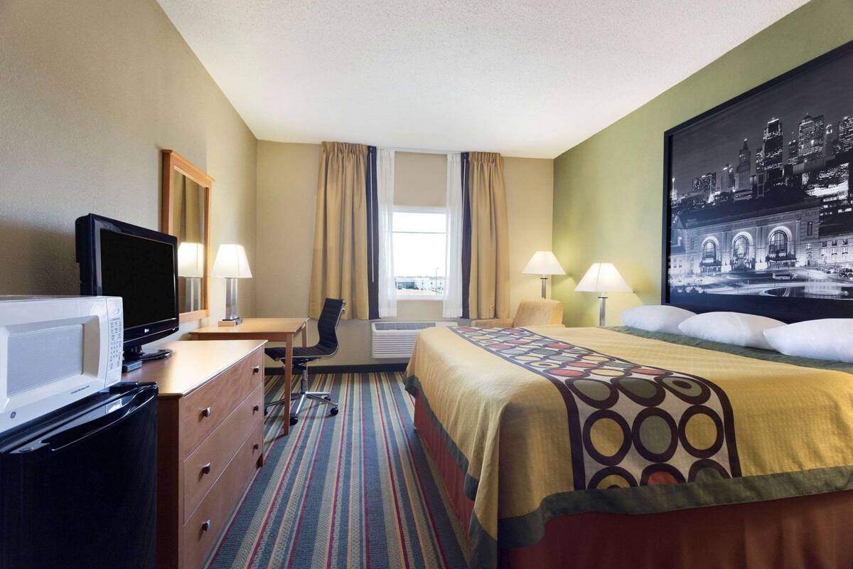 Ein Hotelzimmer mit Bett, Schreibtisch, Stuhl, Fernseher und einem großen Stadtbild an der Wand.