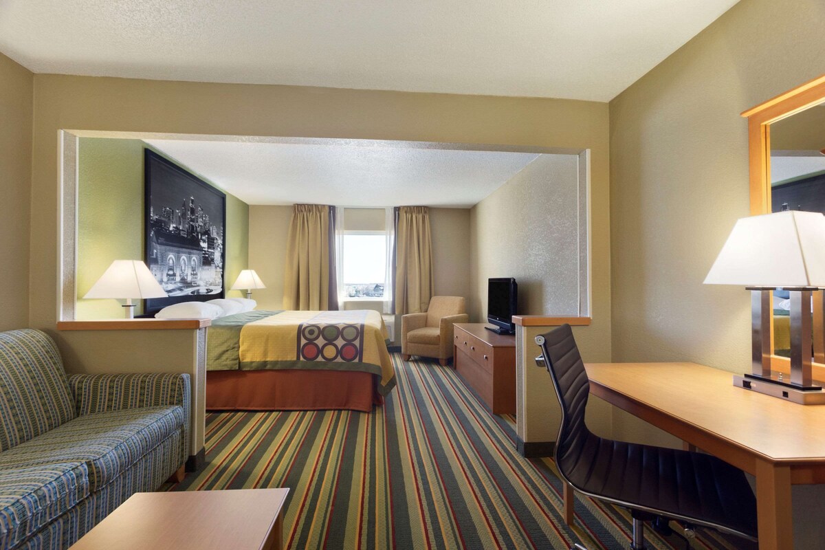 A hotel room with a bed, a sofa, a desk, a chair, a television, and a large mirror.