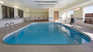 An indoor swimming pool with a tiled floor, a pool ladder, and a seating area with chairs and a table. - Super 8 by Wyndham Lees Summit (Lee's Summit)