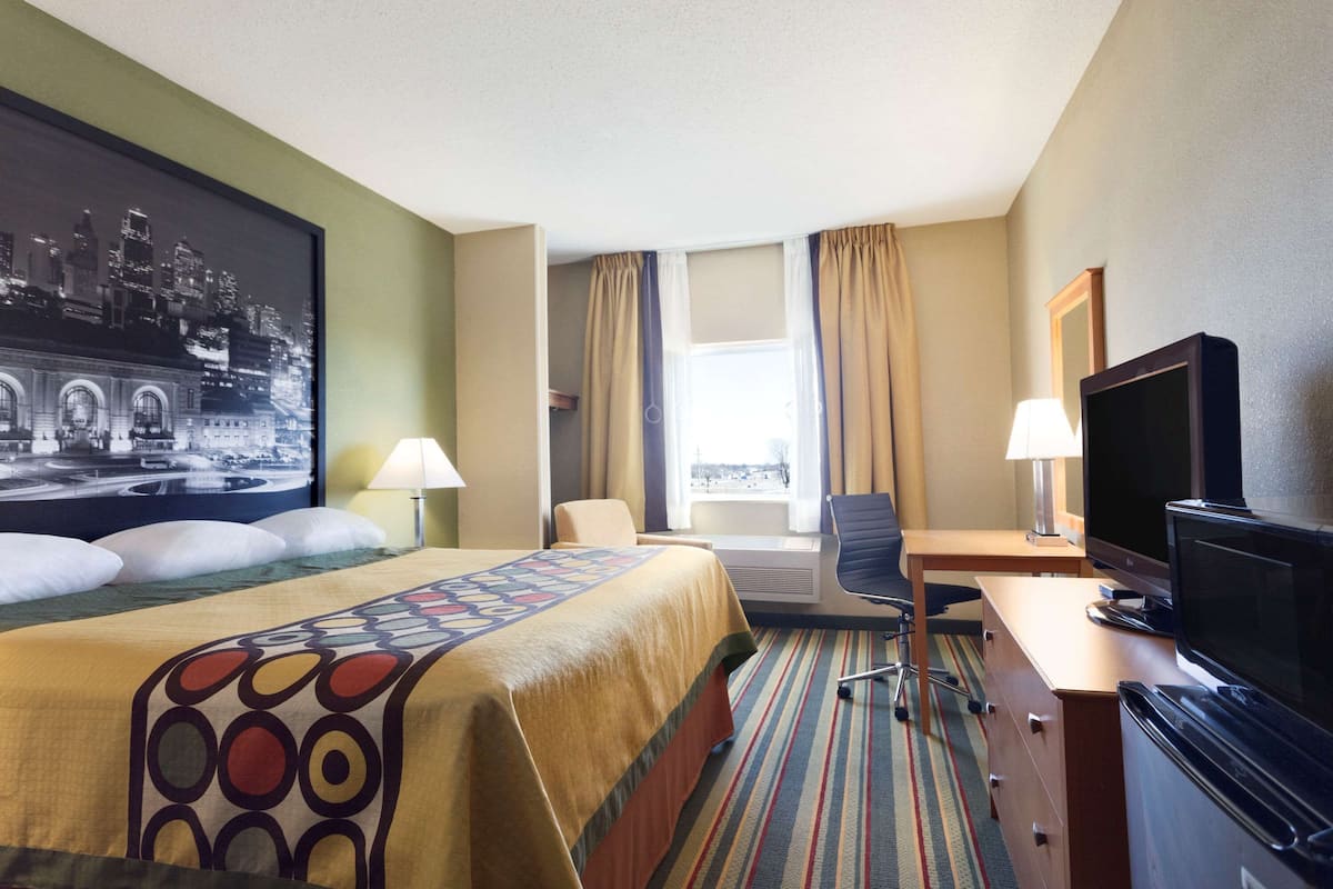 Ein Hotelzimmer mit Bett, Schreibtisch, Fernseher und einem großen Fenster mit Vorhängen.