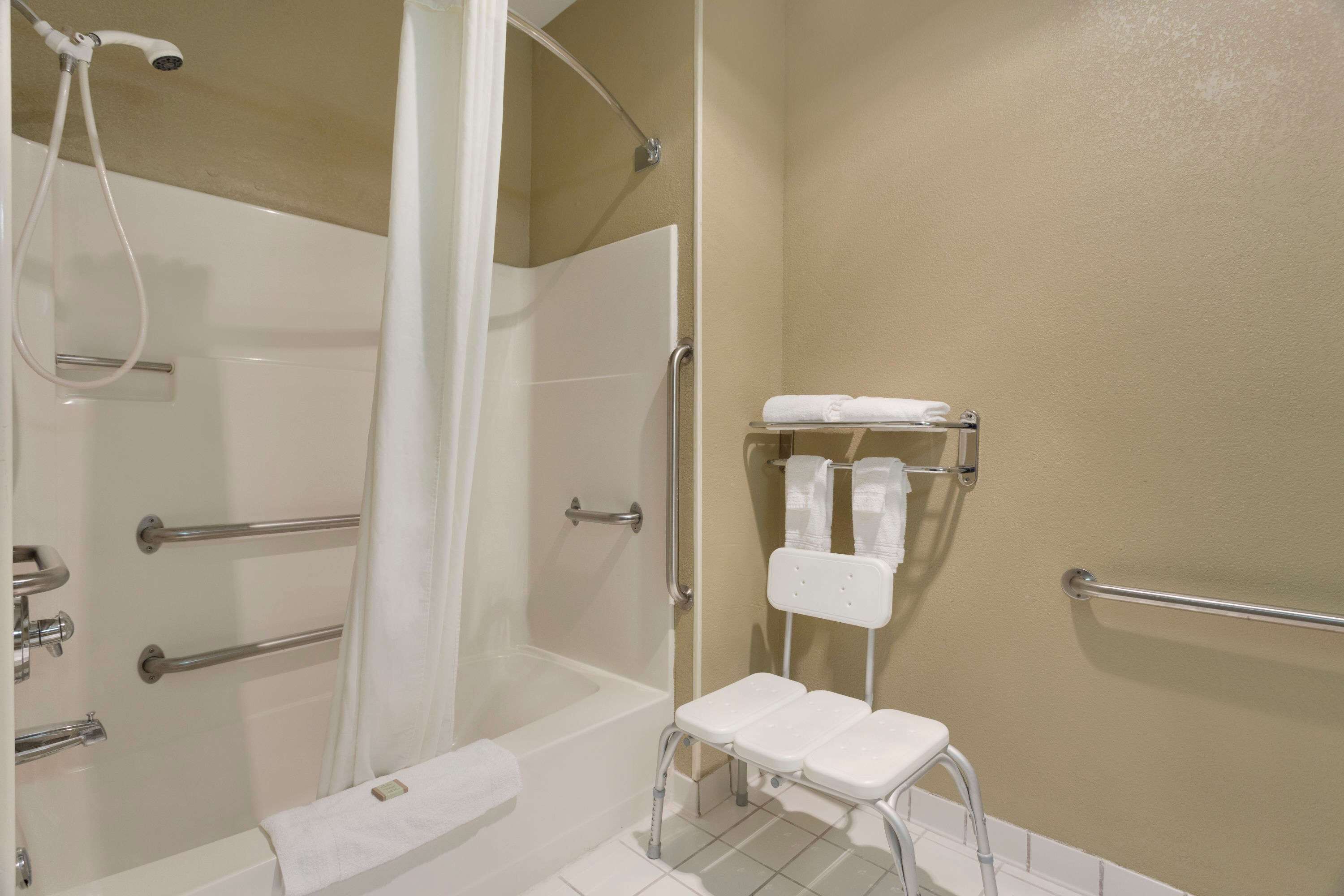 A bathroom with a shower, a toilet, and a small white stool.