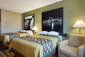 Habitación de hotel con dos camas, una silla, una lámpara y dos obras de arte en las paredes.