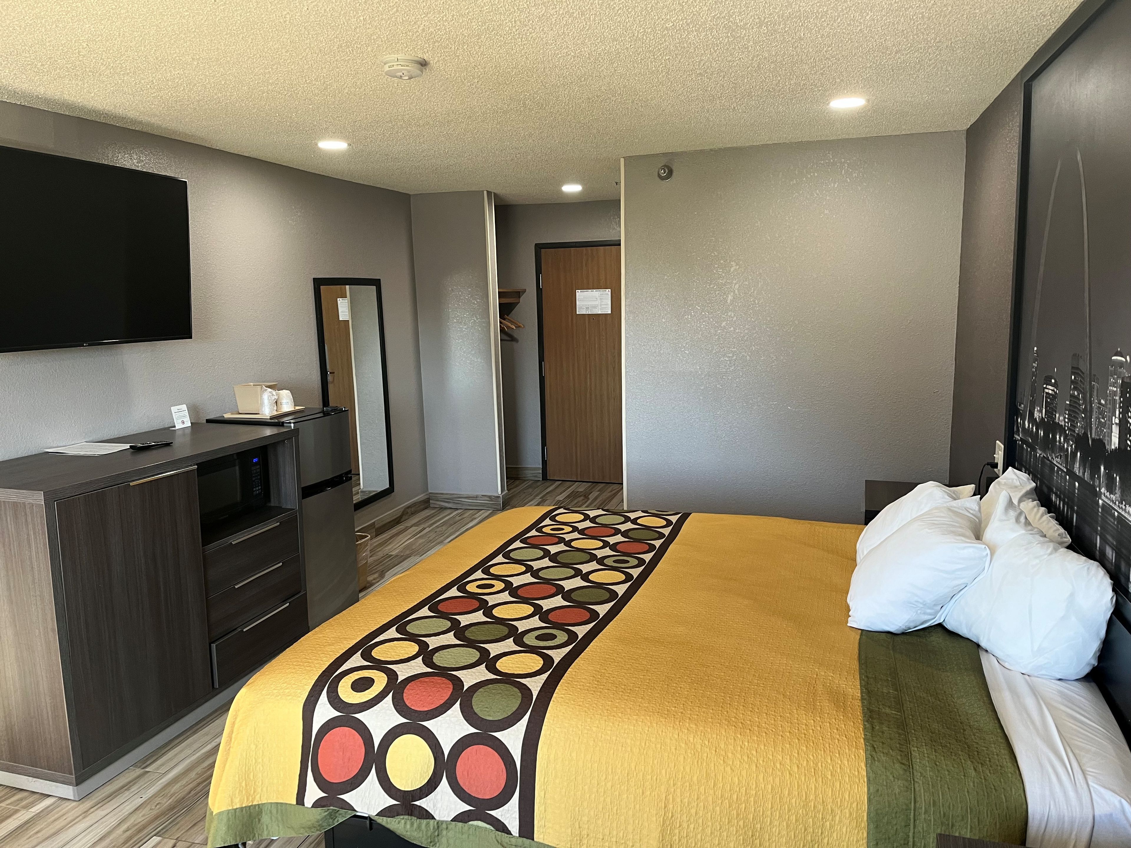 Una habitación de hotel con cama, escritorio, televisor de pantalla plana, microondas y espejo.