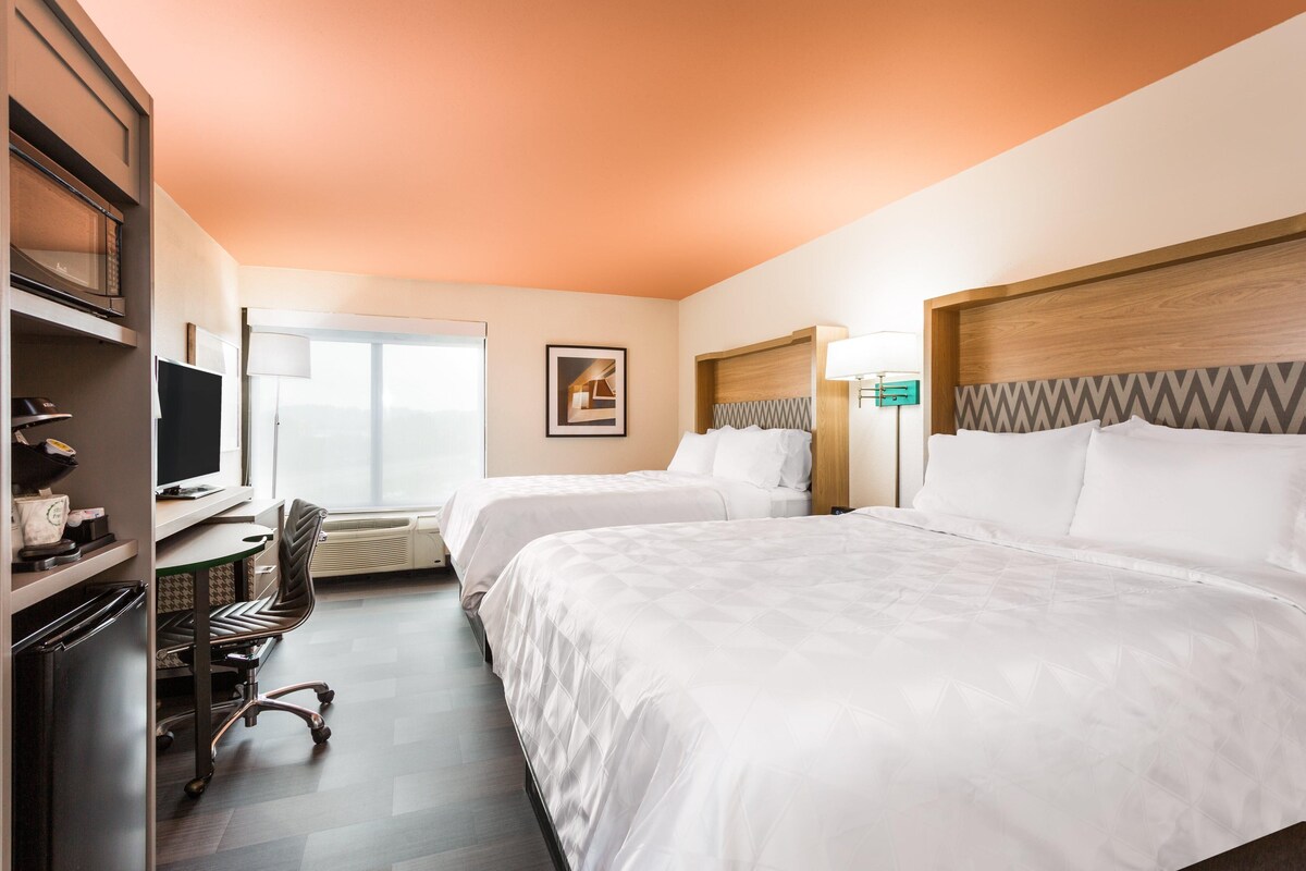 A hotel room with two beds, a desk with a computer, a chair, and a television.