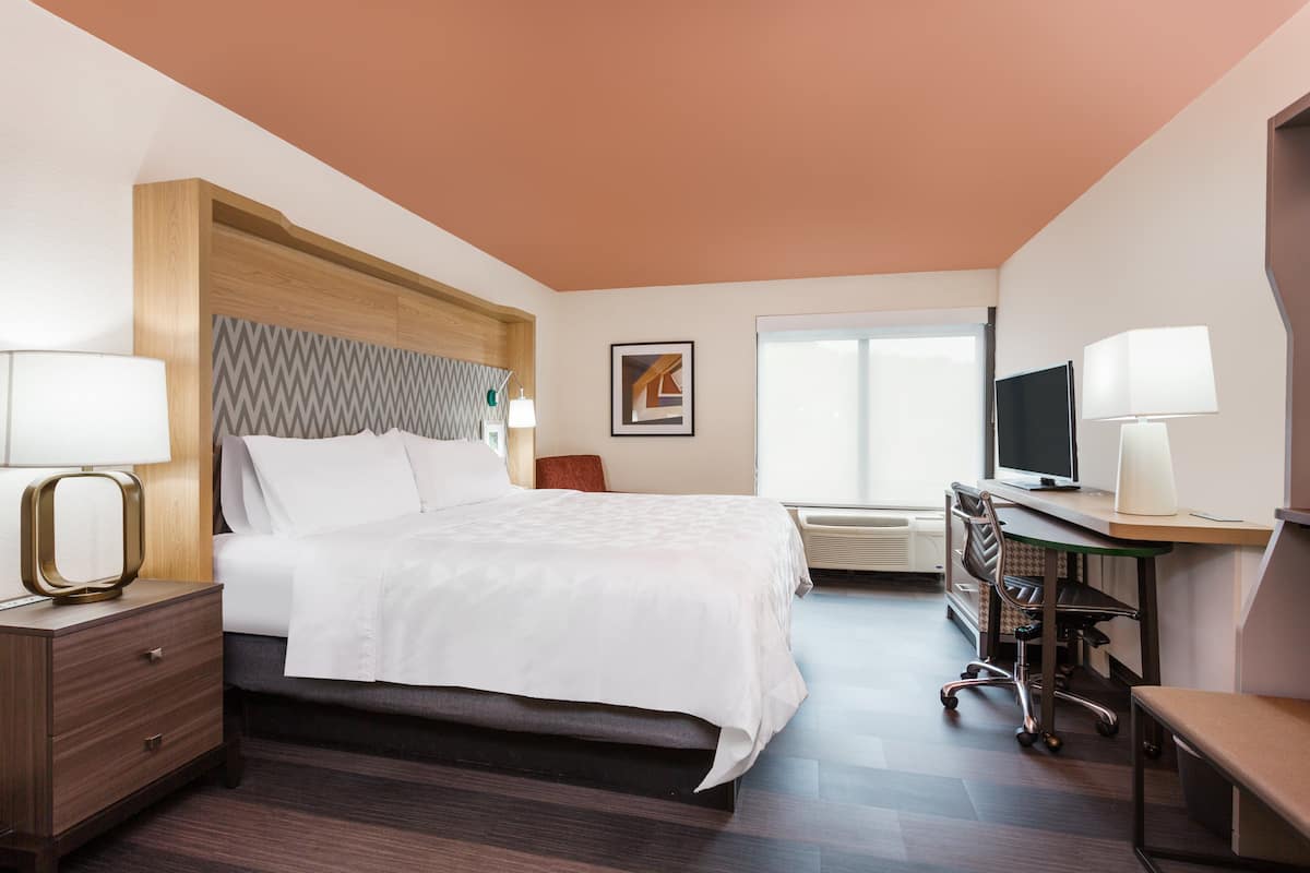 A hotel room with a bed, bedside tables, a desk with a chair, a television, and a window.