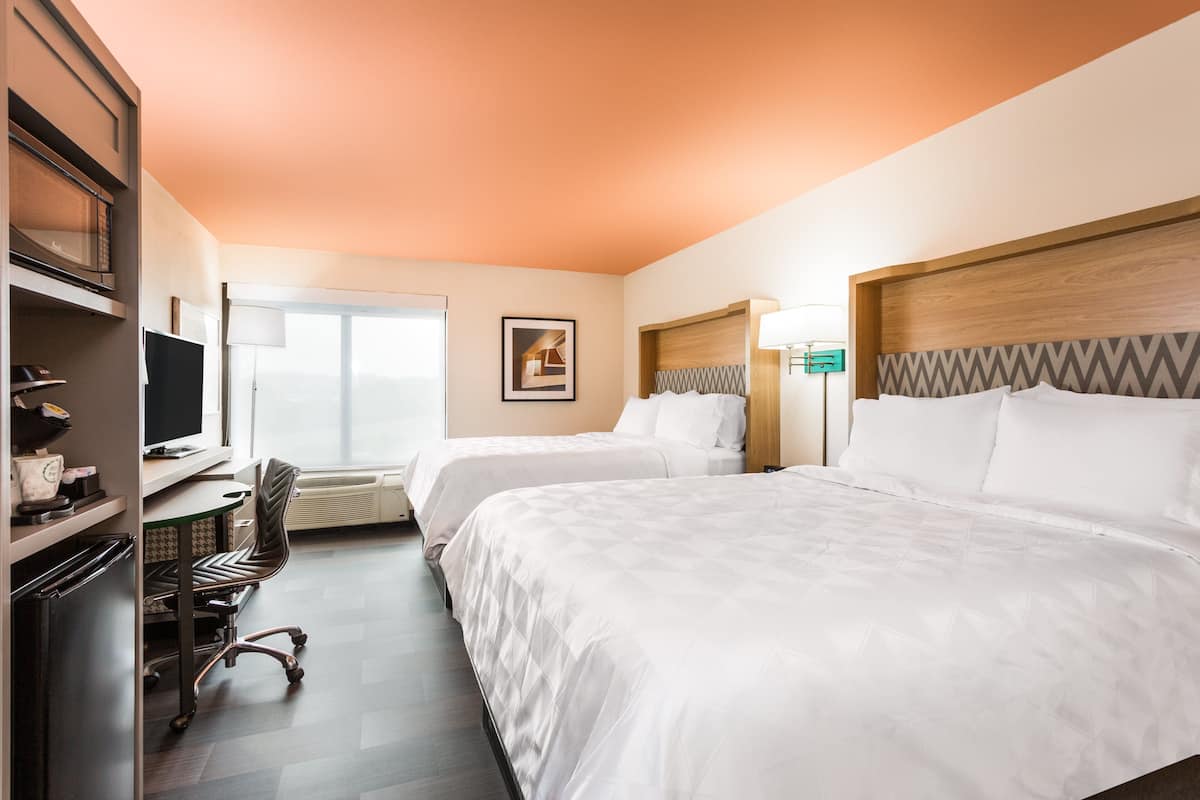 A hotel room with two beds, a desk with a computer, a chair, and a television.