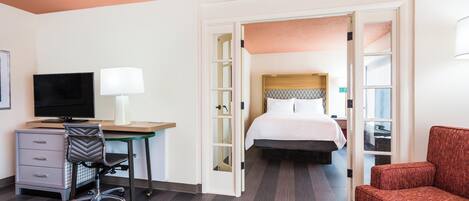 A hotel room with a bed, a desk with a chair, a television, and a red armchair.