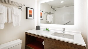 Une salle de bain moderne avec un grand miroir, un lavabo blanc et un porte-serviettes.