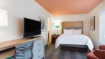 A hotel room with a bed, a TV, a desk with a chair, a nightstand, and a lamp.