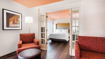 A hotel room with a bed, two armchairs, a round ottoman, a floor lamp, and a framed picture on the wall.