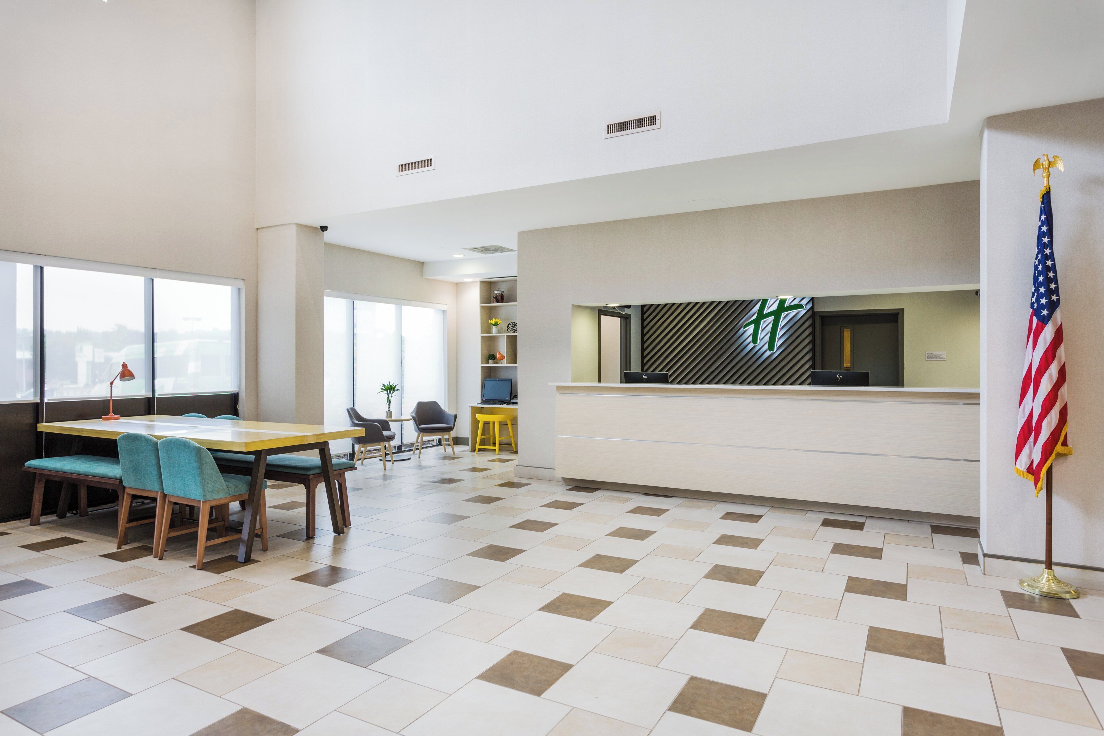 A hotel lobby with a reception desk, a flag, and a seating area with tables and chairs.
