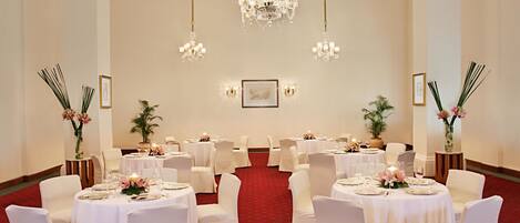 A banquet hall with round tables, white chairs, and chandeliers.