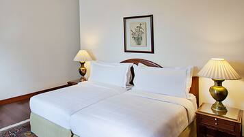 A neatly made bed with white linens, two bedside lamps, a framed floral artwork on the wall, and a patterned rug on the floor.