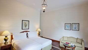 A hotel room with a large bed, a sitting area with a sofa, and a small table with fruit.