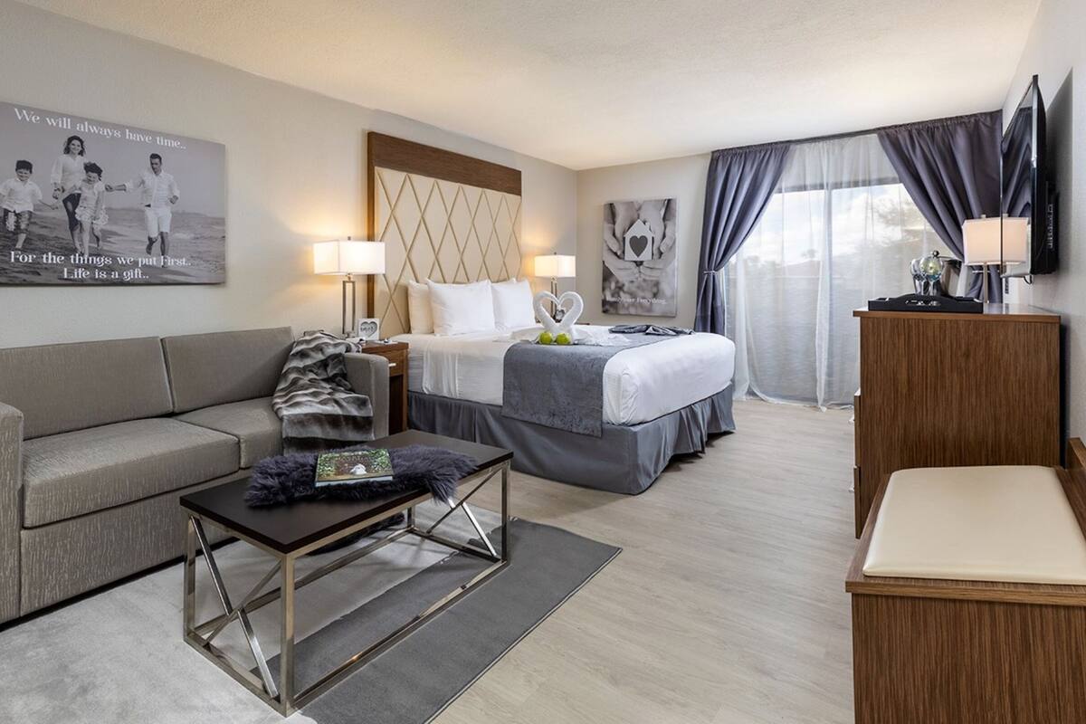 A hotel room with a bed, a sofa, a coffee table, a TV, and a poster on the wall.