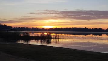 Un atardecer sobre un lago tranquilo con una pequeña construcción en primer plano.