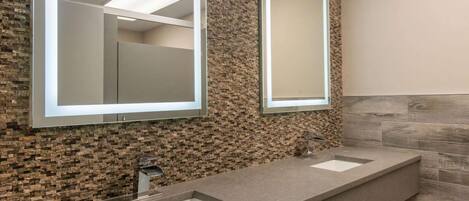 Une salle de bain moderne avec deux lavabos, un grand miroir et un mur à texture.