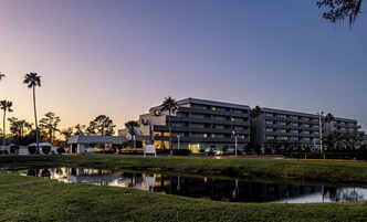 A multi-story hotel with a modern architectural design, featuring a flat roof and a large parking area.
