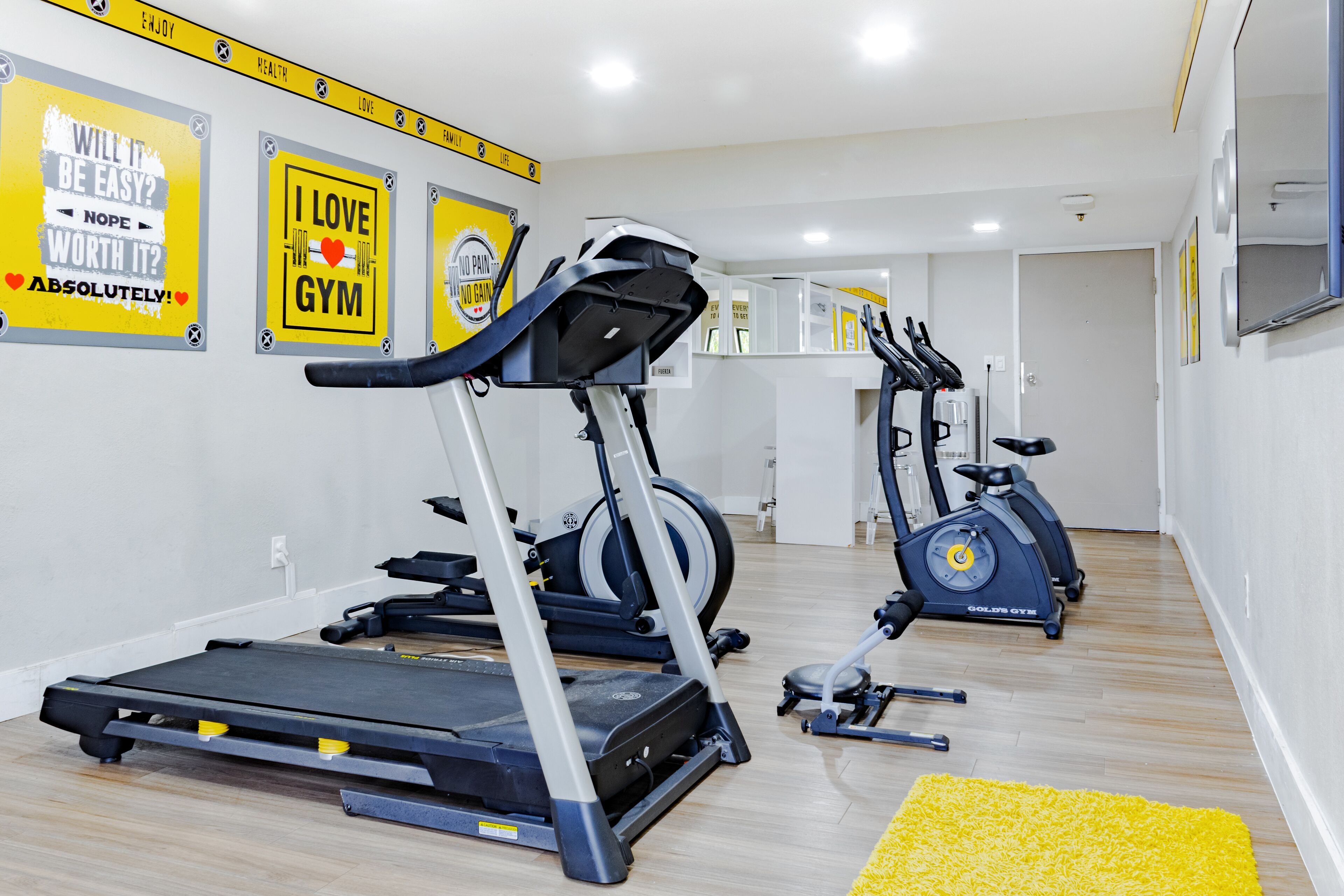 Un gimnasio con cintas de correr, elíptica y bicicleta estática.