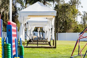 Una carpa blanca con estructura metálica, rodeada de un área de césped con juguetes de plástico de colores.