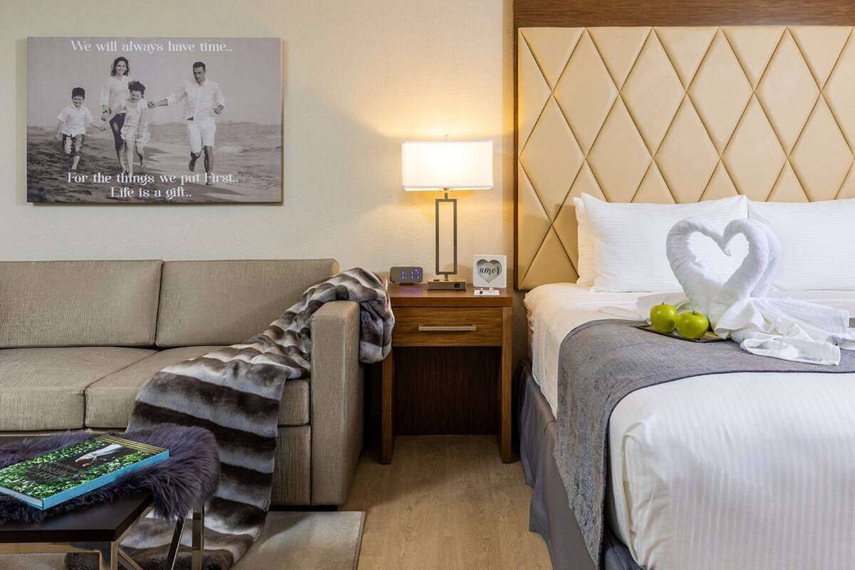 A hotel room with a bed, a nightstand, a lamp, a framed photo on the wall, and a couch.