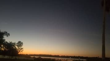 Um pôr do sol sobre águas calmas, com uma linha de costa distante e uma estrutura alta à direita.