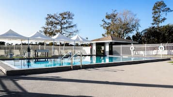 Una piscina con un deck amurallado, sillas de descanso y tiendas blancas al fondo.
